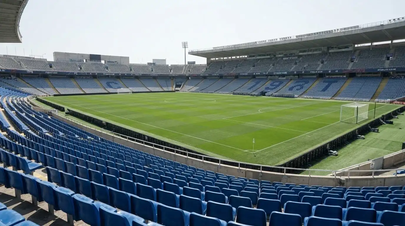 Ein leeres Fußballstadion bei Tageslicht von der Tribüne aus gesehen, der Rasen zeigt gleichmäßige Mähstreifen.